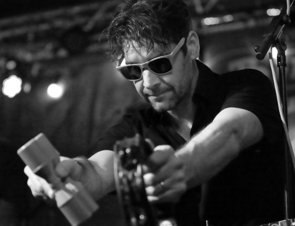 Black and white photo of percussionist pointing shaker and tambourine at the crowd