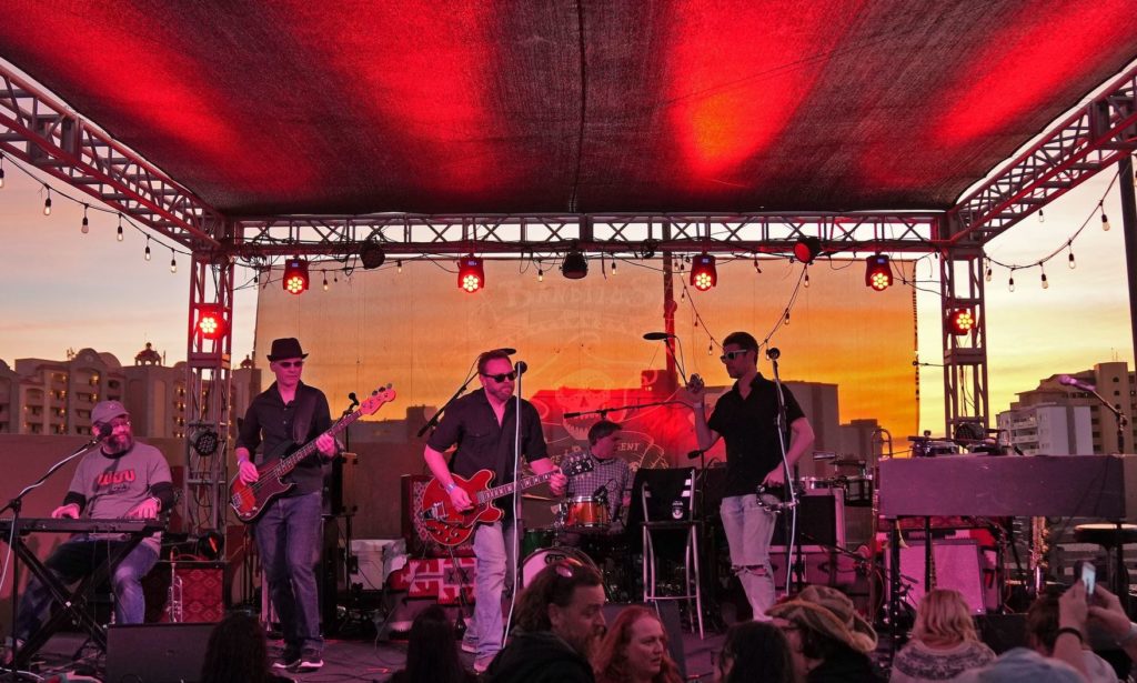 Five band members on outdoor stage at sunset