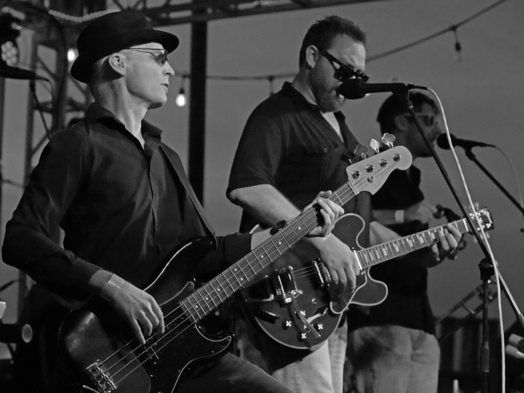 Black and white photo of bassist, guitarist, and singer on an outdoor stage