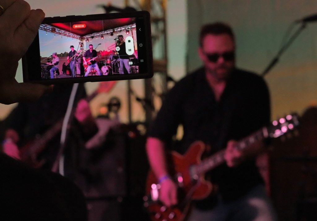 Photo of a mobile phone being used to record video of a band on an outdoor stage